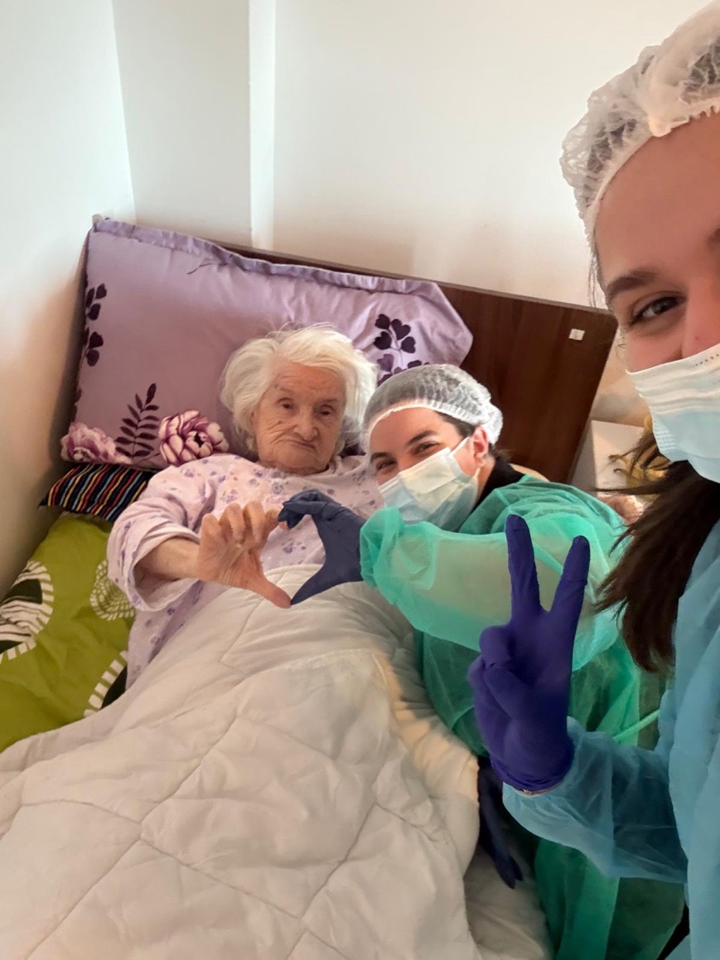 Voluntare alături de o pacientă vârstnică, formând împreună o inimă cu mâinile