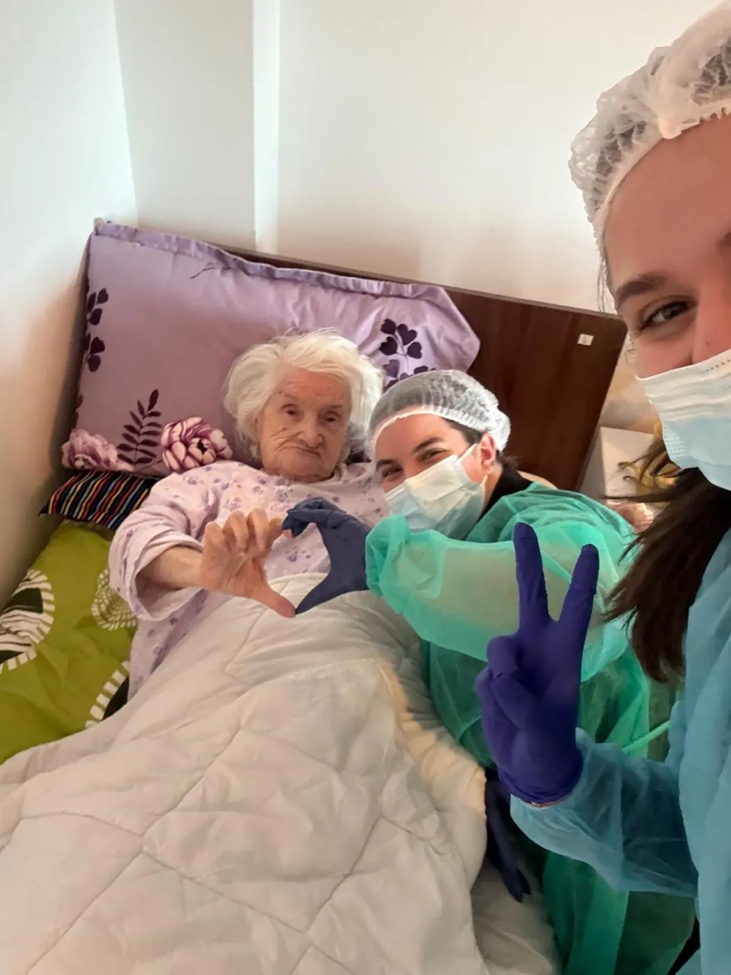 Voluntare în echipament medical și o rezidentă a Căminului de bătrâni Gherghiței formând împreună o inimă cu mâinile